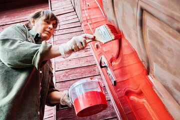 Flat brush used by professional painter for application of metal paint on entrance metal door of rural house, scene shows painting in progress.