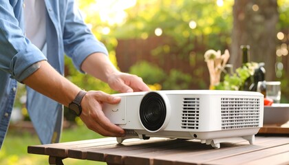 Man setting up a projector outdoors on a patio table, ready for an outdoor movie night.