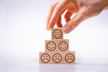Man's hand builds a pyramid of wooden cubes with smiling and sad faces, representing psychology,...