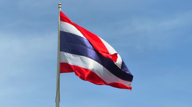 The Thai national flag waving in the breeze on a tall flagpole, set against a bright and cloudless blue sky in Bangkok, symbolizing national pride and identity.