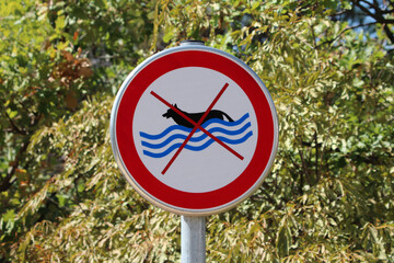 A circular red-bordered sign with a crossed-out swimming dog pictogram signals that dogs are not...