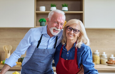 Portrait of happy senior mid aged mature couple prepering meal with fresh vegatebles in kitchen at...
