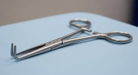 Silver Surgical Clamp on Light Blue Surface in Medical Setting with Sharp Focus Detailed Silver Metal Tool