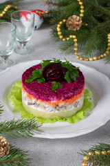 Holiday salad Herring under fur coat on white plate on gray background, decorated with rose from beets