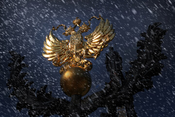 Russia's golden double-headed eagle coat of arms, framed by winter snowfall at night. Symbolizes...