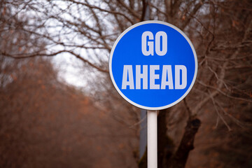 Blue roadside sign, 'GO AHEAD' inscription, city park setting. Powerful motivation concept, encouraging progress and action