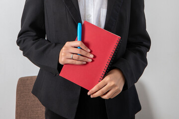 Businesswoman in black suit holding red book in hands.