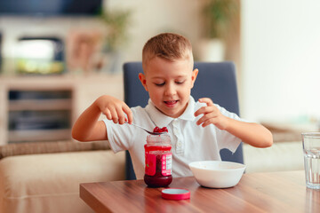 Cute 5-year-old boy having breakfast at home, eating porridge with jam.
