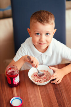 Cute 5-year-old boy having breakfast at home, eating porridge with jam.