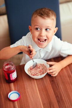 Cute 5-year-old boy having breakfast at home, eating porridge with jam.