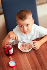 Cute 5-year-old boy having breakfast at home, eating porridge with jam.