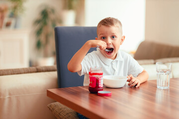 Cute 5-year-old boy having breakfast at home, eating porridge with jam.