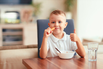 Emotional boy eating sausage at home