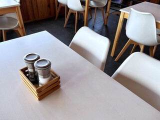 Salt and pepper shakers on a restaurant table with white chairs