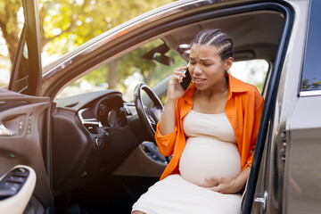Worried black pregnant woman on phone outside car, likely calling for help. Captures urgency,...