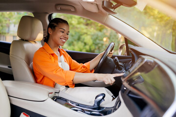 Young black woman interacting with car screen while driving, smiling and relaxed. A modern and...