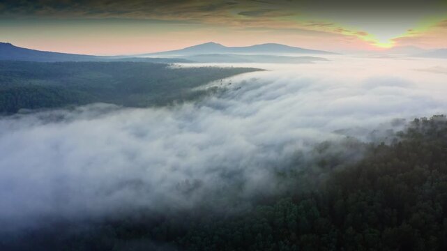 Sunrise illuminating clouds above a forest and mountain range creates a breathtaking natural landscape