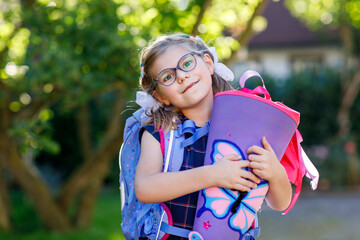 little girl with glasses and a blue backpack, dressed in a navy uniform, holds a colorful school cone called Schultuete and backpack. Happy child smiling, ready for her first day of school