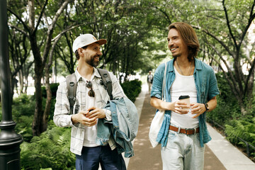 Adult men in stylish casual clothes strolling in city under trees, enjoying small talk, colleagues...