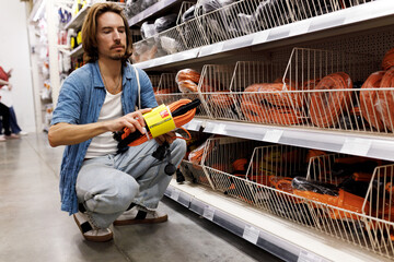 Indoor image of stylish handsome man of 30s with long hair squatting in hardware store choosing...