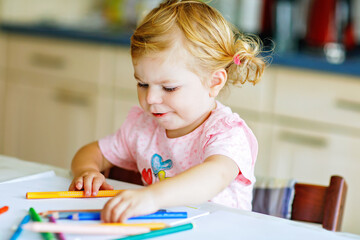 Cute adorable baby girl learning painting with pencils. Little toddler child drawing at home, using...