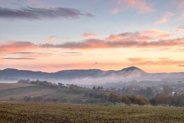 Serene landscape with rolling hills shrouded in mist, painted by a vibrant sunrise sky. Beautiful light