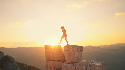 Runner leaps between rocky peaks at sunrise, symbolizing endurance and achievement. Golden light...