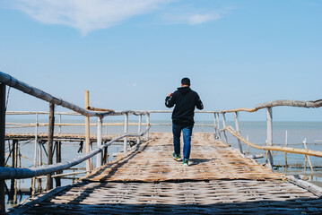 man seen from behind walking on a bamboo bridge leading to the sea
