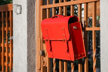 Bright red leather mailbox hanging on a decorative metal gate, showcasing vibrant color contrast...