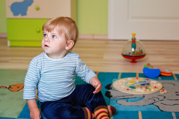 Little toddler boy crawling in playroom, playing with toys. Happy baby having fun indoors. Real...