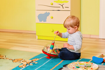 Little toddler boy crawling in playroom, playing with toys. Happy baby having fun indoors. Real...