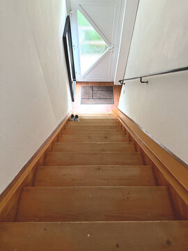 Holztreppe im Innenbereich, die in einen hellen Bereich f&uuml;hrt. 
