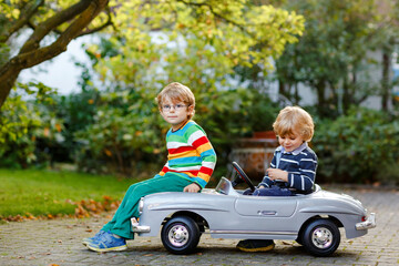 Two little preschool boys playing with big old toy car in summer garden, outdoors. Happy children...
