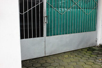 Modern metal gate with green and grey panels and hexagonal paving