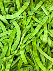 A bunch of green beans are piled on top of each other. They are all green and are in a pile