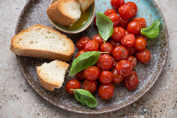 Ciabatta, roasted cherry tomatoes and fresh basil on a brown plate, horizontal shot, middle closeup, selective focus