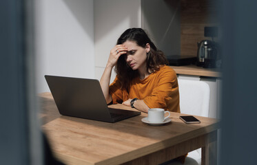 Serious thoughtful sad woman sitting at home working on laptop