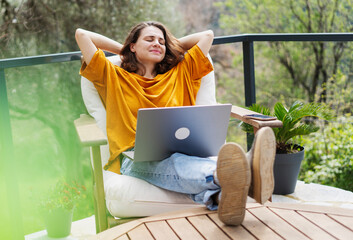 woman sitting on cottage terrace with sea view using laptop in summertime, online work