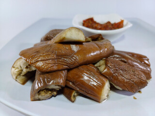 A dish of cooked eggplant slices, served with a vibrant red chili sauce, presented on a rectangular white plate. Suggests a savory, flavorful, and spicy meal, characteristic of Southeast Asian cuisine
