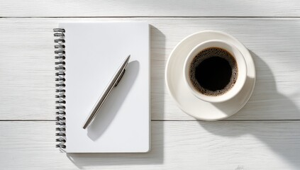 A spiral-bound notebook, pen, and coffee cup on a white wooden surface, bathed in sunlight