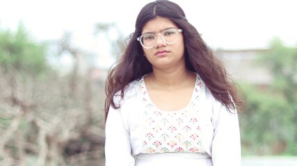 15-year-old girl wearing spectacles sitting alone, looking sad and thoughtful, lost in deep thinking, emotional moment captured in a natural outdoor setting - Powered by Adobe