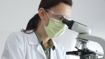 Female professional scientist examining specimen, placing slide under microscope while wearing...