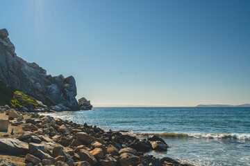 Rocky shoreline meets the ocean under a clear blue sky with distant birds.