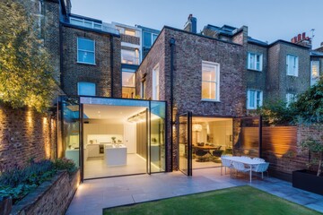 Modern glass extension and backyard of a stylish urban home in London during twilight, showcasing contemporary design and open living spaces