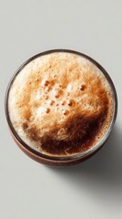 An overhead shot captures a rich, foamy dark soda in a clear glass, presenting a refreshing and fizzy beverage against a simple, clean background design concept.