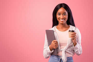 Attractive black lady with laptop computer and takeaway coffee looking at camera on pink studio...
