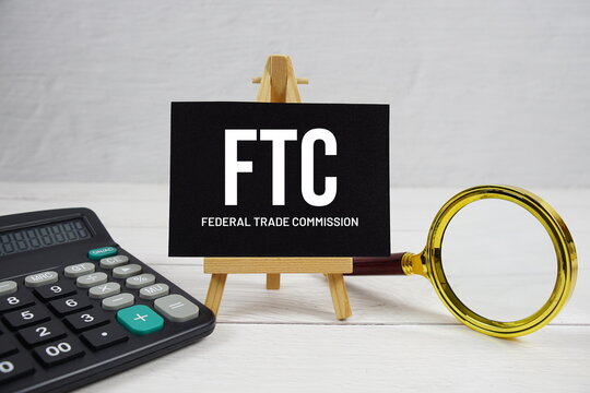 FTC abbreviation of Federal Trade Commission text with magnifying glass and calculator on wooden background