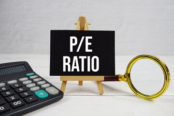 P/E abbreviation of Ratio acronyms Price-To-Earnings text with magnifying glass and calculator on...