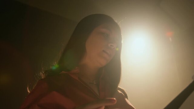 Low angle tilt-up close-up shot of young actress gesturing gently with her arms while practicing her acting performance in dimly lit studio