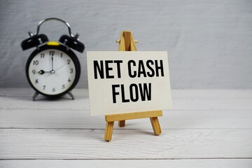 Net Cash Flow text with easel and alarm clock on wooden background